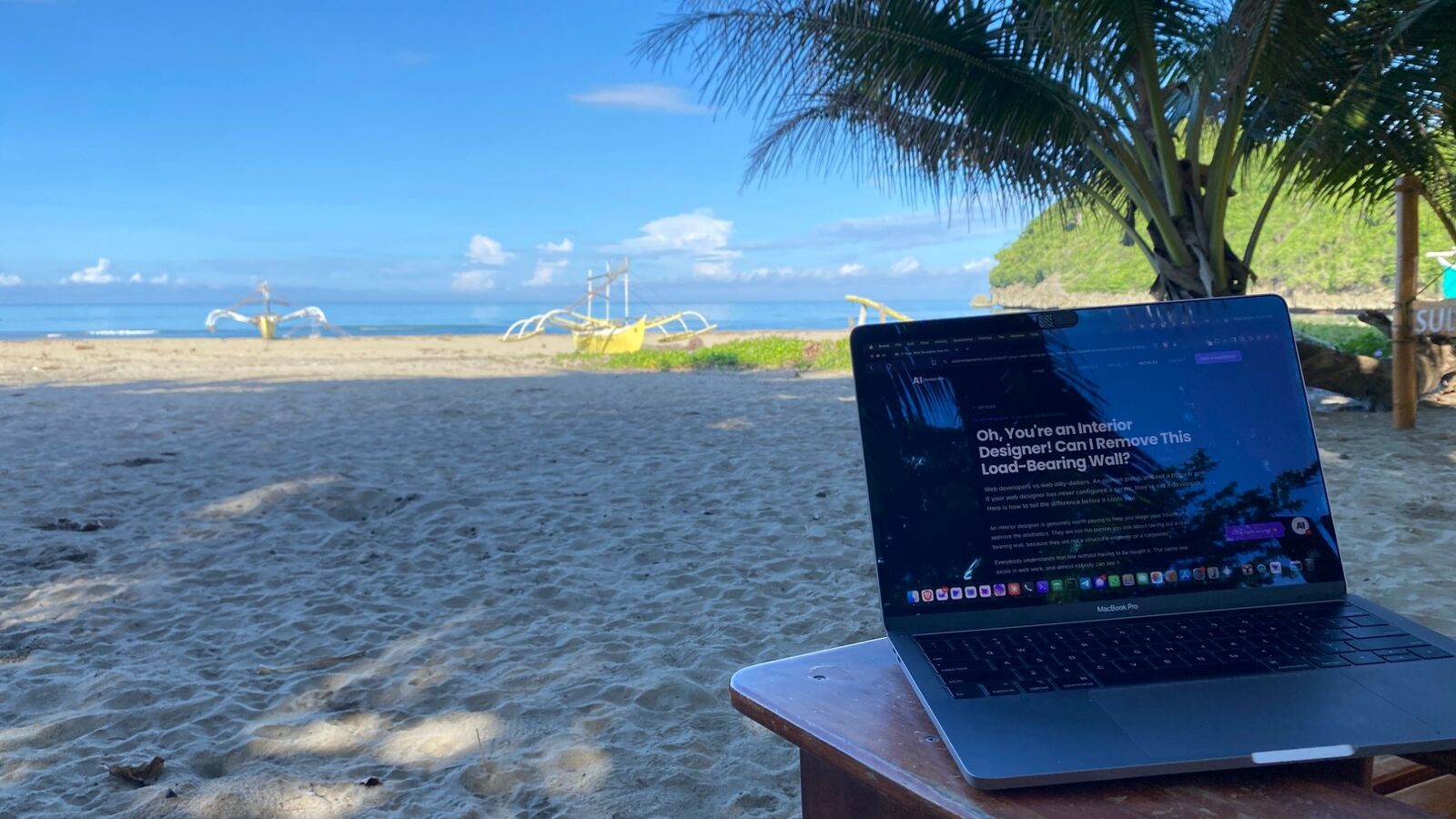 A MacBook Pro on a wooden table on a tropical beach, showing this article on aidevelopments.nz, with outrigger boats and palm trees behind